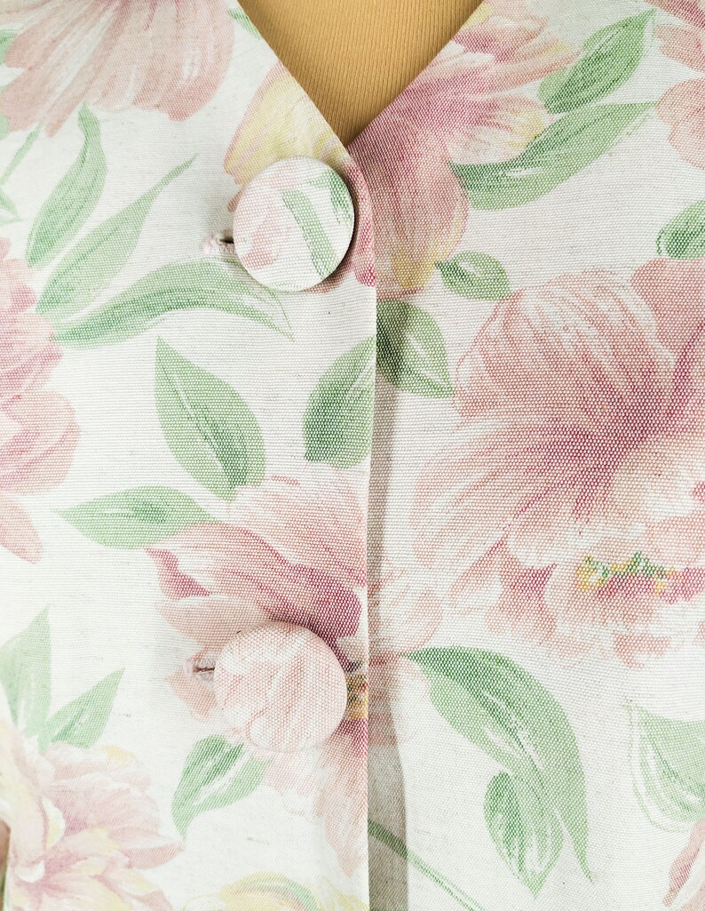 May include: A white fabric with a floral pattern in shades of pink, green, and yellow. The fabric has two large buttons.