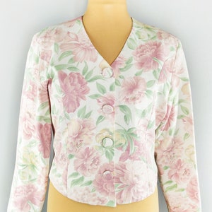 May include: A white floral print blazer with a v-neck and button closure. The blazer has a pink and green floral pattern.