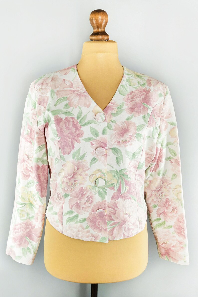 May include: A white floral print blazer with a v-neck and button closure. The blazer has a pink and green floral pattern.