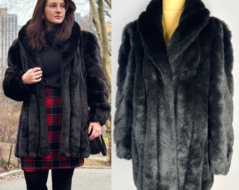 May include: A black faux fur coat with a long, straight cut and a wide collar. The coat has a button closure and is made of a soft, plush fabric.