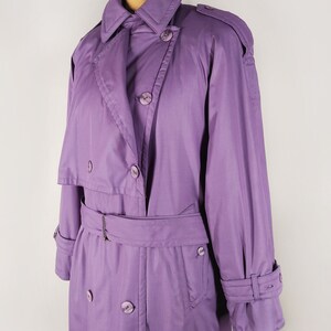 May include: A long, purple raincoat with a double-breasted closure, a belt, and a storm flap. The raincoat has a classic trench coat style.