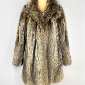 May include: A full-length, vintage fur coat in shades of brown and gray. The coat features a wide collar and long sleeves. The fur appears soft and luxurious, with a natural, textured appearance. The coat is displayed on a mannequin.