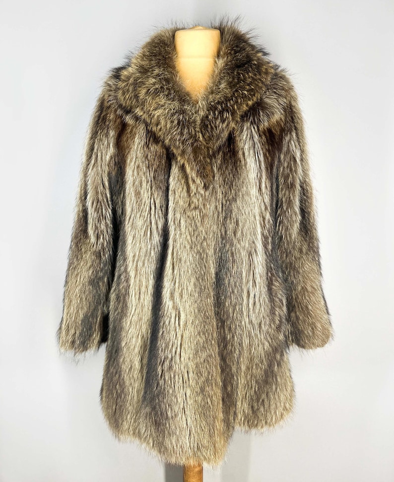 May include: A full-length, vintage fur coat in shades of brown and gray. The coat features a wide collar and long sleeves. The fur appears soft and luxurious, with a natural, textured appearance. The coat is displayed on a mannequin.