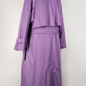 May include: A long purple raincoat with a belt and button closures. The raincoat has a stand-up collar and long sleeves.