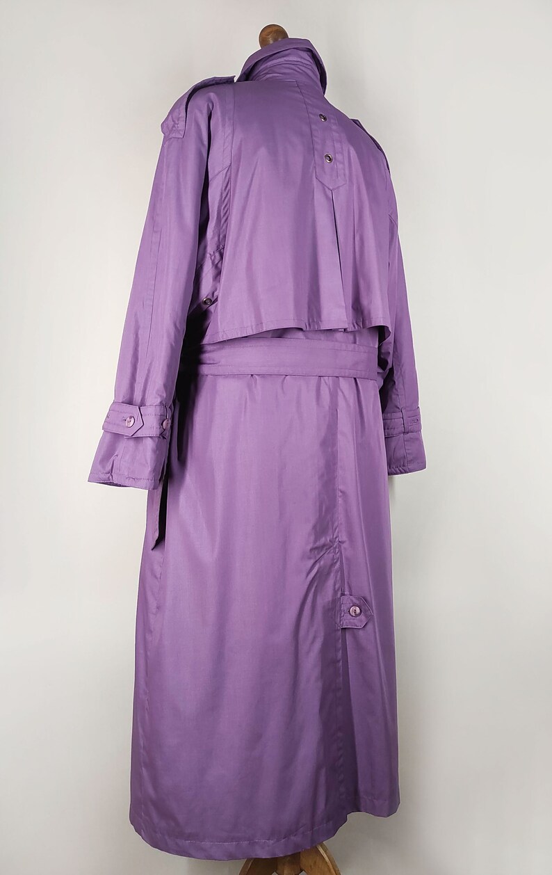 May include: A long purple raincoat with a belt and button closures. The raincoat has a stand-up collar and long sleeves.