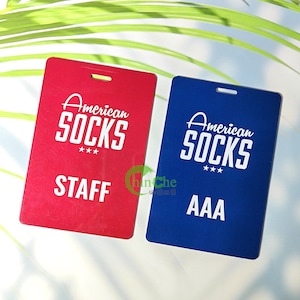Może przedstawiać: Dwie prostokątne plastikowe tabliczki z zaokrąglonymi rogami. Tabliczka po lewej stronie jest czerwona z białym tekstem, kt&oacute;ry brzmi "American Socks" i "Staff". Tabliczka po prawej stronie jest niebieska z białym tekstem, kt&oacute;ry brzmi "American Socks" i "AAA".