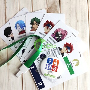 Może przedstawiać: Zestaw białych plastikowych kart z postaciami z anime. Karty zawierają tekst "Olimpijski Sportowiec" i "Japonia". Jest też zielony sznurek z białym klipsem i okrągły guzik z wielokolorową grafiką przedstawiającą ludzi i glob. Guzik ma napis "Herbalife Nutrition".