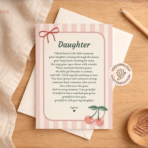Op de afbeelding: Een wenskaart met een roze gestreepte rand en het woord "Daughter" bovenaan. De kaart bevat een gedicht en is versierd met een rode strik en een kersenillustratie. Een potlood en een houten kom zijn ook zichtbaar.