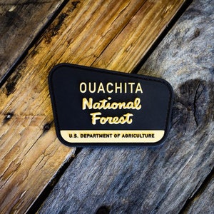 May include: Black and gold embroidered patch with the text "Ouachita National Forest" and "U.S. Department of Agriculture".