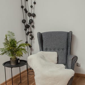 May include: A gray armchair with a white faux fur throw draped over it. The chair is in a room with a wooden floor and a plant in a pot on a black metal side table.
