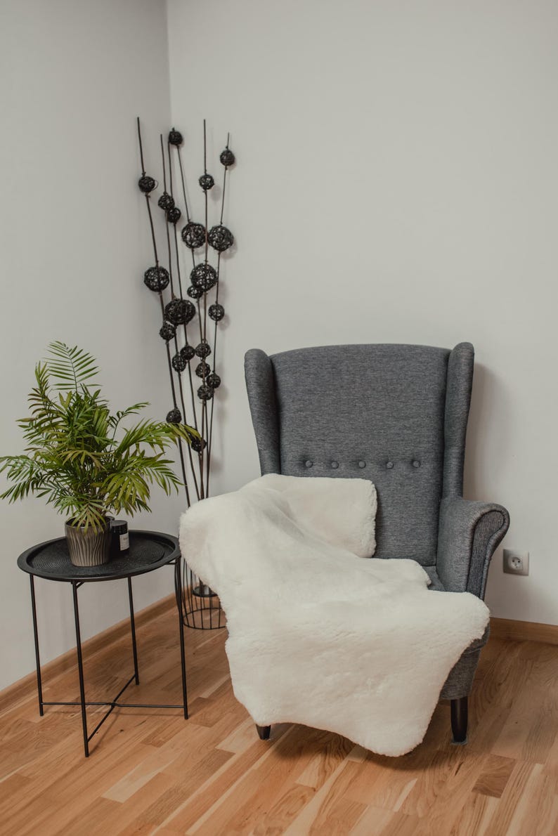 May include: A gray armchair with a white faux fur throw draped over it. The chair is in a room with a wooden floor and a plant in a pot on a black metal side table.