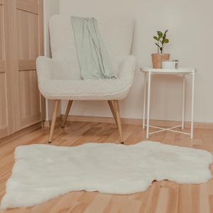 May include: A white fluffy rug with a white armchair and a small white side table with a plant in a woven basket on top. The chair has a light green throw draped over the back.