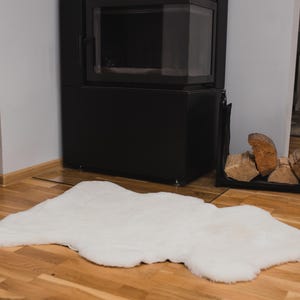 May include: A white faux fur rug on a wooden floor in front of a black fireplace.