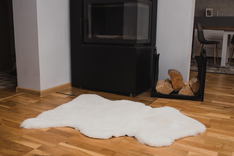 May include: A white faux fur rug on a wooden floor in front of a black fireplace.