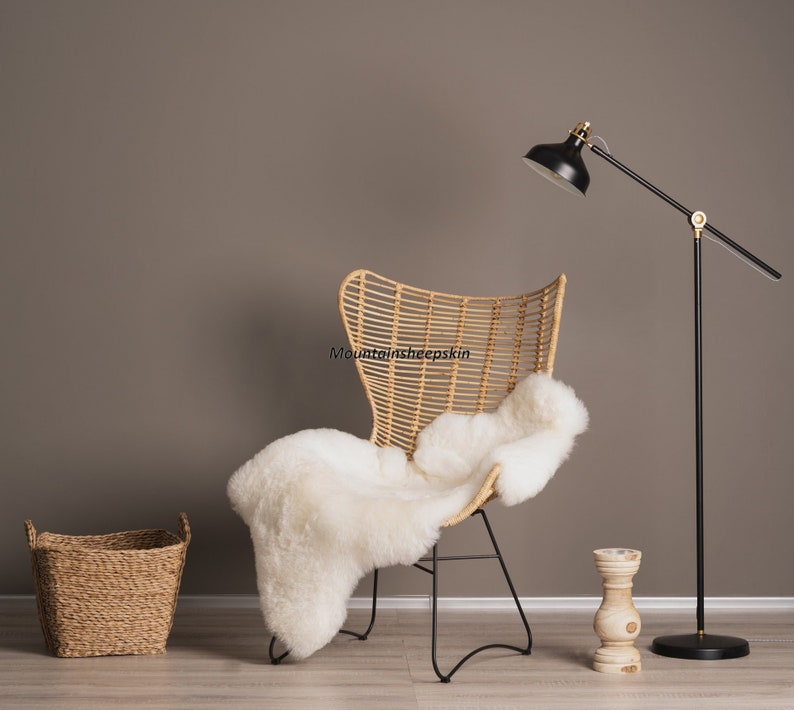 May include: A wicker chair with a white sheepskin throw draped over it. A black floor lamp with a gold accent stands to the right of the chair. A small woven basket sits on the floor to the left of the chair.