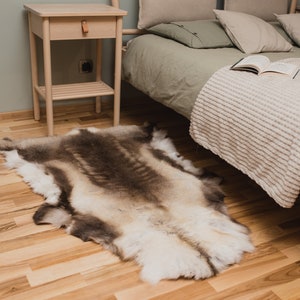 K&ouml;nnte beinhalten: Ein wei&szlig;er und brauner Rentierfellteppich auf einem hellen Holzboden neben einem Bett mit einer gr&uuml;nen Bettdecke und einer wei&szlig;en Wolldecke.