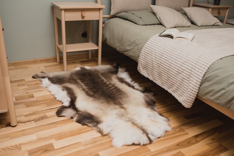K&ouml;nnte beinhalten: Ein wei&szlig;er und brauner Rentierfellteppich auf einem hellen Holzboden neben einem Bett mit einer gr&uuml;nen Bettdecke und einer wei&szlig;en Wolldecke.