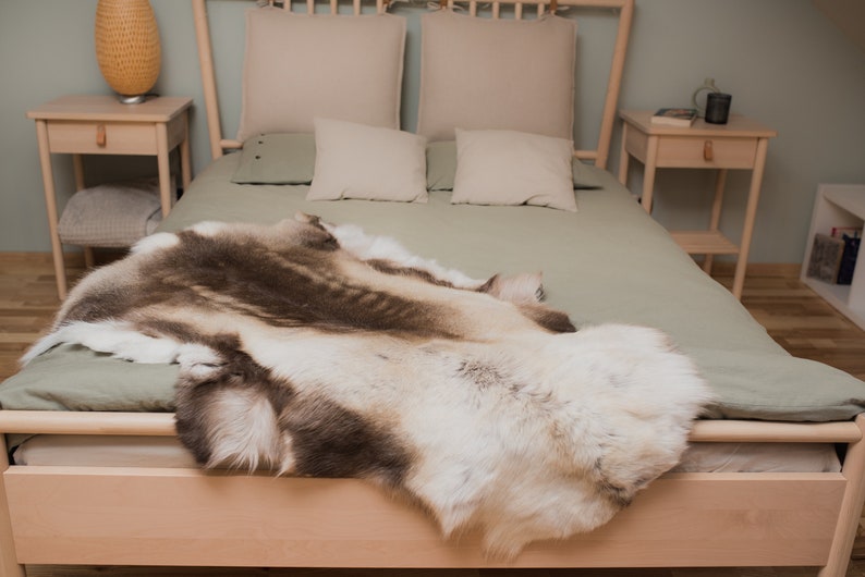 K&ouml;nnte beinhalten: Ein hellgr&uuml;nes Bett mit einem wei&szlig;en und braunen Rentierfell darauf. Das Bett hat einen Holzrahmen und zwei Holz-Nachttische.