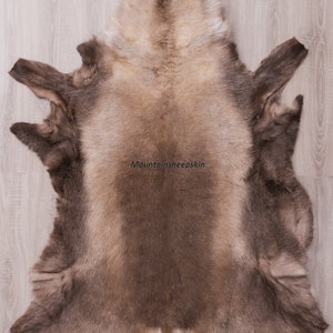K&ouml;nnte beinhalten: Ein gro&szlig;er, hellbrauner Schaffellteppich mit weicher, flauschiger Textur. Der Teppich liegt flach auf einem Holzboden. Der Text "Mountainsheepskin" ist in der Mitte des Teppichs gedruckt.