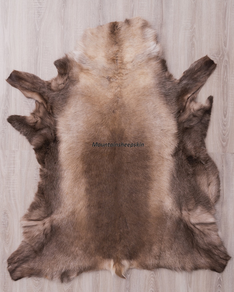 K&ouml;nnte beinhalten: Ein gro&szlig;er, hellbrauner Schaffellteppich mit weicher, flauschiger Textur. Der Teppich liegt flach auf einem Holzboden. Der Text "Mountainsheepskin" ist in der Mitte des Teppichs gedruckt.