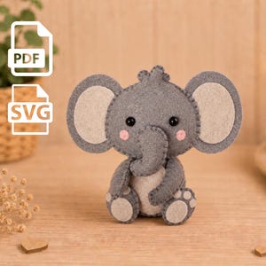 May include: A handcrafted felt elephant plush toy featuring a dark gray body, light gray inner ears, a light gray belly, and light gray foot pads. The elephant has black bead eyes, pink stitched cheeks, and a curled trunk, with PDF and SVG icons.
