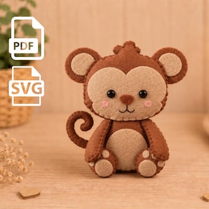 May include: A felt monkey plush toy featuring dark brown and beige fabric, black bead eyes, a stitched nose and mouth, and pink blush accents on the cheeks. The monkey has a curled tail, rounded ears, and a circular beige patch on its belly.