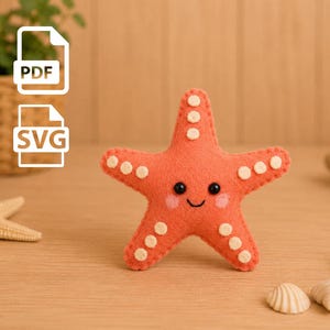 Op de afbeelding: Een koraalkleurige vilten zeester knuffel met een geborduurde glimlach, twee zwarte kraaloogjes, roze blosjes op de wangen en kleine crèmekleurige cirkelvormige vilten accenten op elk van de vijf armen. De afbeelding bevat PDF- en SVG-bestandsiconen.