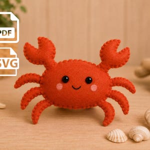 Op de afbeelding: Een feloranje vilten krab knuffel met zwarte kraaloogjes, een geborduurde glimlach en roze ronde wangen. De krab heeft twee opgeheven scharen en zes poten, met zichtbare stiksels langs de randen van het afgeronde lichaam.
