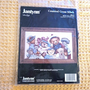 May include: A Janlynn Counted Cross Stitch kit featuring a framed image of a group of teddy bears. The finished size is 16" x 8" (40.6 x 20.3 cm). The kit includes 14-count cotton Aida fabric, 6-strand cotton floss, beads, needles, graph, and instructions.