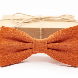 May include: A burnt orange bow tie made of linen fabric. The bow tie is tied and ready to wear.