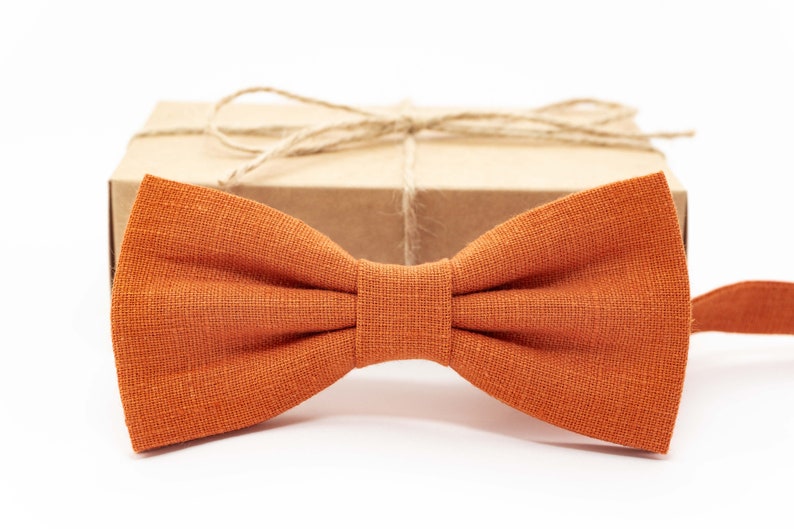 May include: A burnt orange bow tie made of linen fabric. The bow tie is tied and ready to wear.