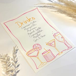 May include: A white rectangular menu card featuring a pink hand-drawn border and the word Drinks in orange calligraphy. The list includes Espresso Martini, Margarita, Mimosa, Aperol Spritz, Cosmopolitan, Mojito, and Gin & Tonic with cocktail illustrations.