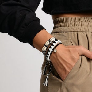 Op de afbeelding: Een vrouw draagt een zwart getailleerd topje en een kaki cargo broek met een trekkoord. Ze draagt een wit en zwart kralen armbandje om haar pols.