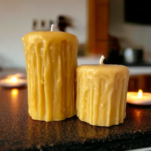 May include: Two yellow beeswax candles with a drippy, textured finish. The candles are unlit and have white wicks.