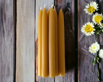 May include: A group of six yellow beeswax candles on a wooden surface. The candles are arranged in a row and are all the same size.