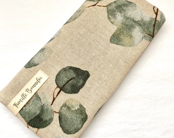 May include: A beige fabric eyeglass case with a green eucalyptus leaf print. The case has a brown leather tag with the text "Famille Bommeler" printed on it.