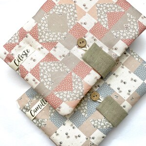 Peut inclure: Deux carnets recouverts de tissu avec un motif patchwork dans des tons de rose, gris et blanc. Les carnets ont une fermeture à bouton et une sangle en tissu. Le carnet du haut porte le nom "Celeste" et le carnet du bas porte le nom "Camille".