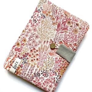 Op de afbeelding: Een clutch van stof met een bloemenpatroon, een knoopsluiting en een riem van linnen. Op de voorkant van de clutch staat "Luce" gedrukt.