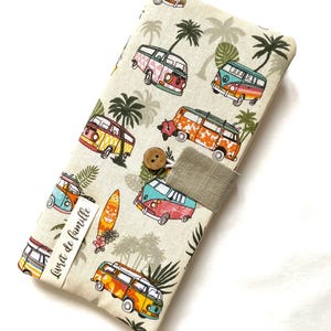 May include: A beige fabric case with a pattern of colourful camper vans, palm trees, and surfboards. It has a button closure and a fabric strap. The text "Livret de famille" is printed on a small label.