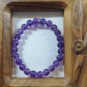 Puede incluir: Un brazalete de amatista púrpura con un acento de cuentas plateadas. El brazalete está hecho de cuentas redondas y está enhebrado en un cordón elástico transparente.