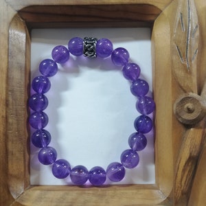 Puede incluir: Un brazalete de cuentas de amatista púrpura con un cierre plateado.