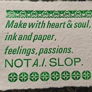 Op de afbeelding: Handgemaakte papieren print met groene tekst: "Make with heart & soul, ink and paper, feelings, passions. NOT A.I. SLOP." De tekst wordt omlijst door decoratieve groene randen.