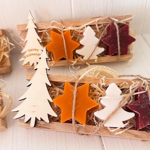 Könnte beinhalten: Weihnachtsgeschenksets. Jede Holzkiste enthält sternförmige Seifen in Orange, Weiß und Burgunder, einen Weihnachtsbaum aus Holz und Stroh. Der Holzbaum trägt den Text "Frohe Weihnachten". Die Kisten sind mit Bindfäden verschnürt.