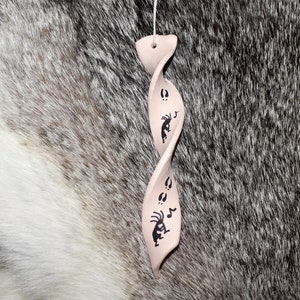 May include: A white ceramic ornament shaped like a spiral with black painted designs of a Native American dancer and footprints.