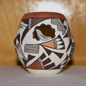 Puede incluir: Una olla de cerámica blanca con un recorte de pájaro y intrincados patrones geométricos en negro, marrón y rosa.