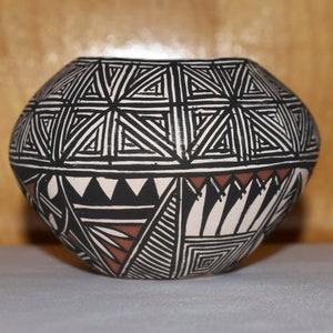 May include: A black and white pottery bowl with geometric designs. The bowl has a red and brown accent around the middle.