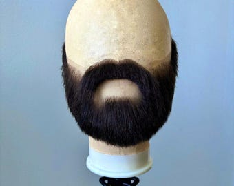 May include: A mannequin head with a dark brown mustache and beard. The head is on a black stand.