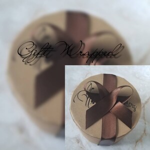 May include: A round, brown gift box with a brown ribbon tied in a bow. The box is wrapped in brown paper and has the words "Gift Wrapped" written on it.