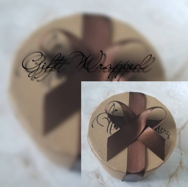 May include: A round, brown gift box with a brown ribbon tied in a bow. The box is wrapped in brown paper and has the words "Gift Wrapped" written on it.
