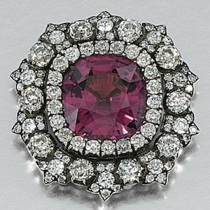Könnte beinhalten: Eine Vintage-Brosche mit einem großen, quadratisch geschliffenen, tiefrosa Edelstein im Zentrum, umgeben von einem Kranz aus kleineren, funkelnden Diamanten. Die Diamanten sind in einem Silber- oder Platinrahmen gefasst, was ein luxuriöses Design ergibt.